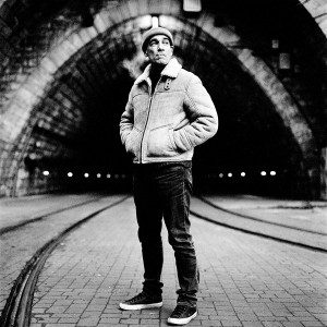 Jean-Marc Barr standing in front of a tunnel smoking cigarette and wearing a jacket.