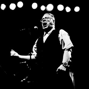 John Lyndon Pil singing to the microphone on the stage at a concert.