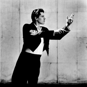 Kevin Griffiths making a conducting pose with a baton in his hand wearing a tuxedo.