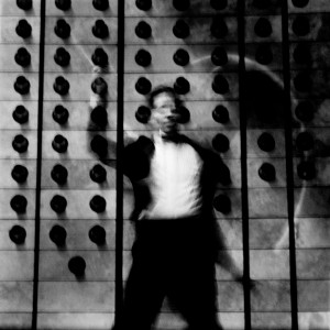 Fuzzy photograph of Kevin Griffiths conducting with the wall with black dots in the background.