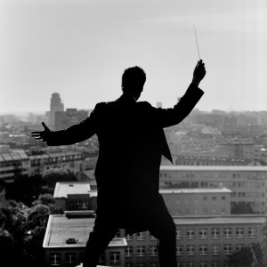 Kevin Griffiths posing from the back on the rooftop of a building with baton in his hand with a city view in the background.