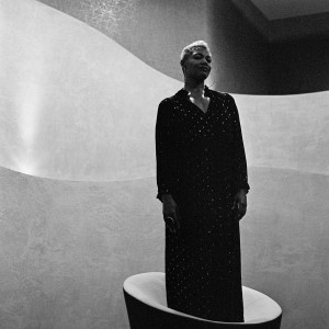 Measha Brueggergosman standing on a chair wearing a dress.