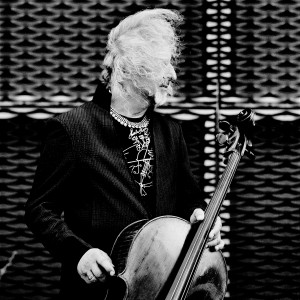 Misha Maisky posing with his cello with hair blown by wind looking to the right.