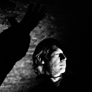 Face of Richard Dorfmeister with shadow of his hand with the brick wall in the background.
