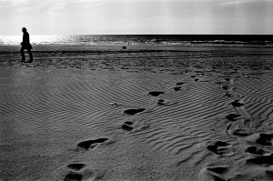 Theo Jansen walking on a beach with foot prints in the sand.